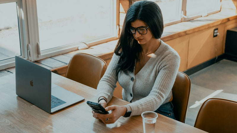 Mujer con gafas mirando el móvil delante del portátil